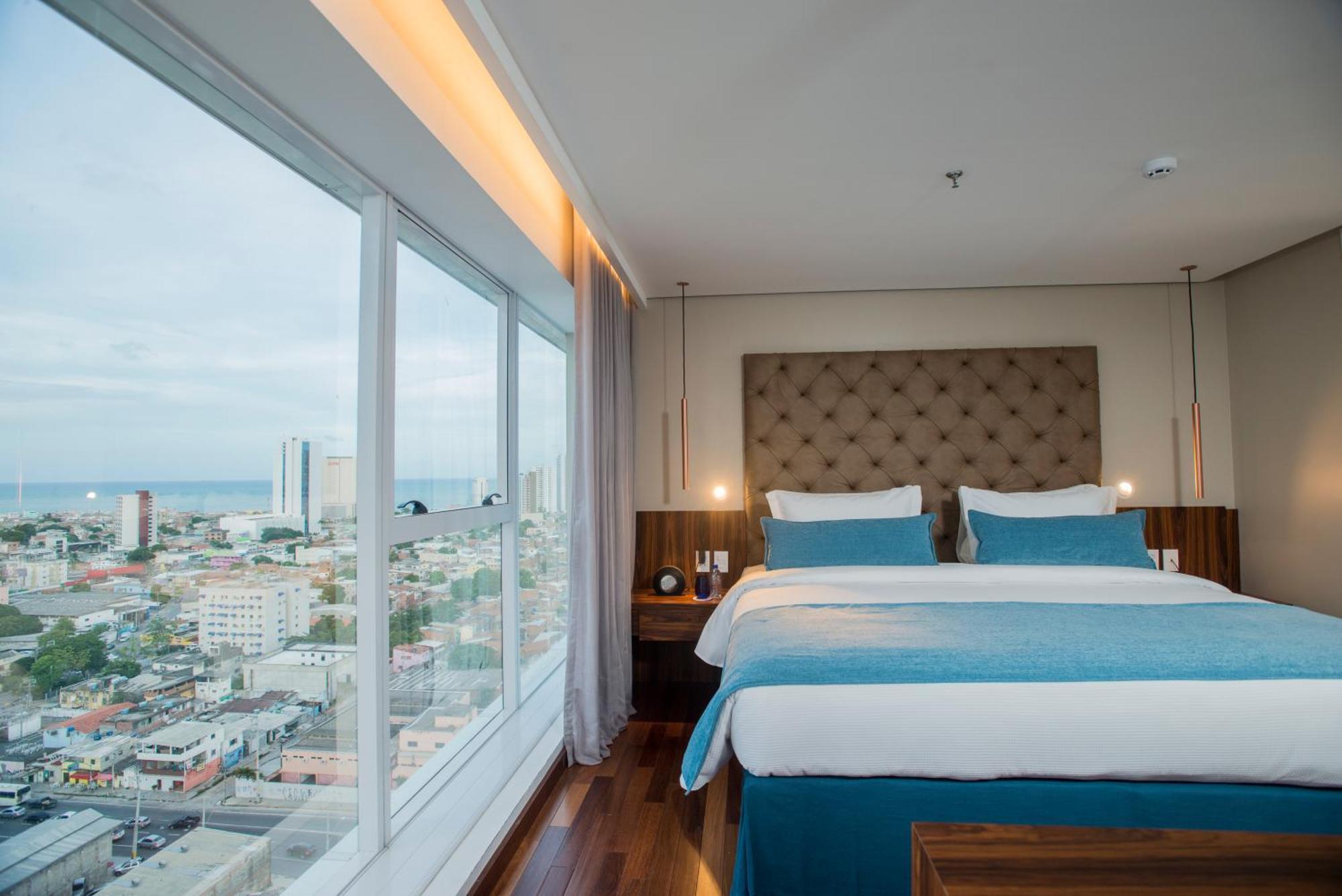 Hotel Luzeiros Ресіфі Екстер'єр фото The photo shows a modern hotel room featuring a large window with a city view. Inside, there are two neatly made beds with light blue and white bedding, flanked by wooden nightstands. The room has a contemporary design, with a padded headboard and so